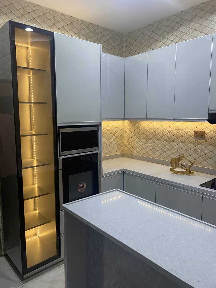 Modern kitchen design in Abuja with sleek white cabinets, minimalist layout, and wood finish island by Forte Aesthetics

