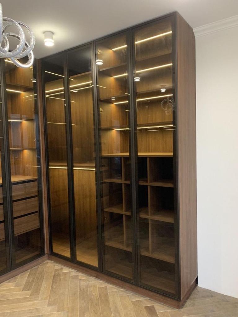 Luxury walk-in closet with glass wardrobe doors and ambient lighting